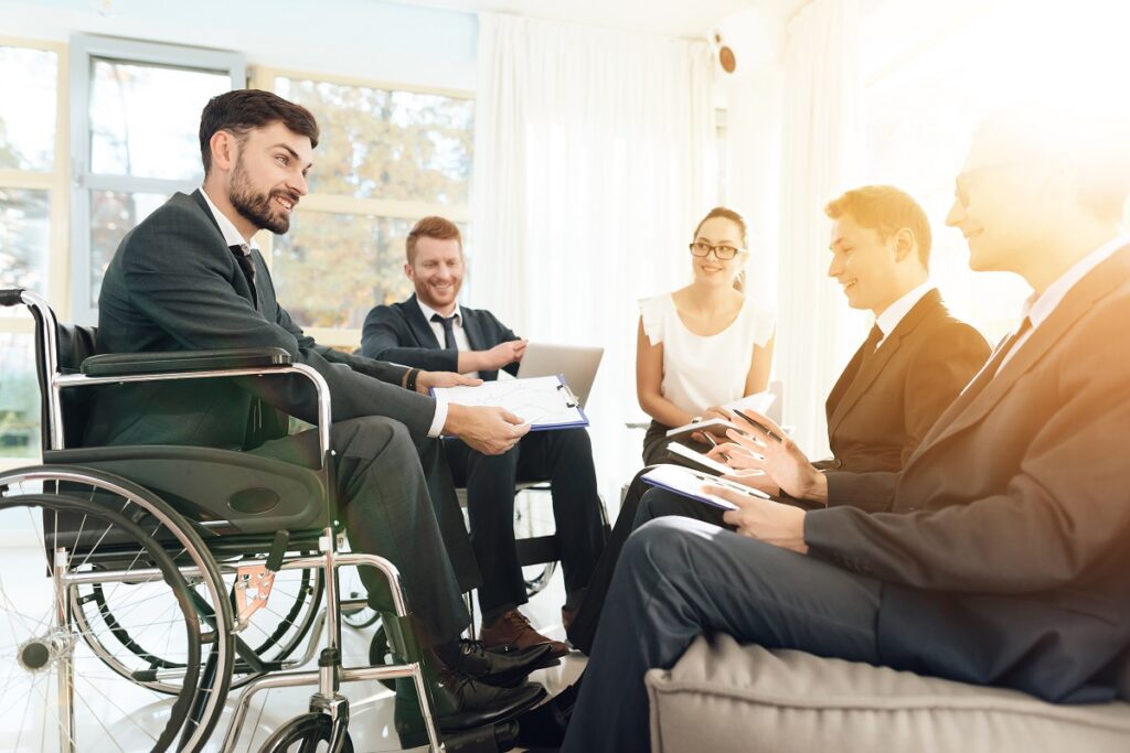 People sitting down and man sitting in wheelchair in a corporate meeting